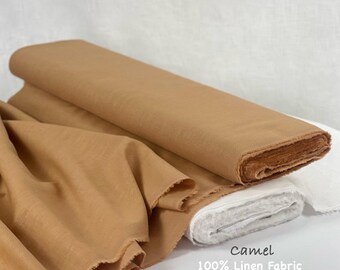 Op de afbeelding: Een rol camelkleurige stof met een deel van het materiaal naar voren gedrapeerd. De stof heeft een zichtbare weefstructuur. De tekst op de afbeelding luidt: Camel 100% Linen Fabric. Het materiaal wordt getoond naast een witte stoffen rol.