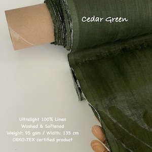 Op de afbeelding: Een rol cedergroene ultralichte 100% linnen stof. De stof is gewassen en verzacht, met een gewicht van 95 g/m&sup2; en een breedte van 135 cm. De tekst "Cedar Green" is zichtbaar op de stof.