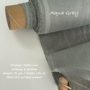 May include: A roll of aqua gray ultralight 100% linen fabric. The fabric is softened and washed, with a weight of 95 gsm and a width of 135 cm. The text "Aqua Gray" is written on the fabric. The product is OEKO-TEX certified.