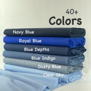 May include: A stack of six folded fabric bolts in various shades of blue, labeled with the text 40+ Colors, Navy Blue, Royal Blue, Blue Depths, Blue Indigo, Dusty Blue, and Clear Sky, arranged from darkest to lightest blue hues.