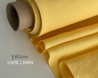 May include: A roll of bright yellow fabric made of 100% linen, featuring a visible woven texture. The fabric is wrapped around a brown cardboard tube, with a portion of the material unrolled to display its drape and consistent solid colour.
