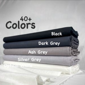 K&ouml;nnte beinhalten: Ein Stapel aus f&uuml;nf gefalteten Stoffballen in einem Farbverlauf, beschriftet mit dem Text 40+ Colors. Die Stofffarben von oben nach unten sind Black, Dark Grey, Ash Grey, Silver Grey und Optical White, alle mit einer sichtbaren Webstruktur.