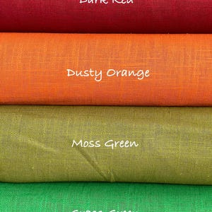 May include: Four stacked rolls of fabric featuring a visible woven texture. The top roll is labeled Dark Red, the second is Dusty Orange, the third is Moss Green, and the bottom roll is labeled Grass Green. Each color is clearly identified by text.