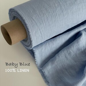 May include: A roll of baby blue 100% linen fabric with a visible woven texture and frayed edges. The fabric is wrapped around a brown cardboard tube. The text Baby Blue 100% LINEN is printed on the left side of the image in a simple font.