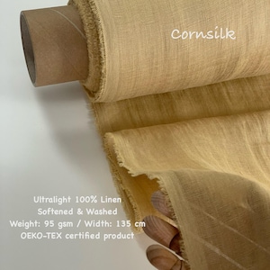 May include: A roll of cornsilk-colored linen fabric. The fabric is ultralight, 100% linen, softened, and washed. The width is 53 inches. The text "Cornsilk" is visible on the fabric. The text "Ultralight 100% Linen, Softened & Washed, Weight: 95 gsm / Width: 135 cm, OEKO-TEX certified product" is also visible.