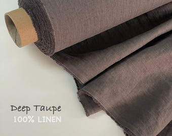 Op de afbeelding: Een rol stof in diep taupe met een zichtbare geweven textuur. De stof is gelabeld als 100% linnen. Het materiaal is om een kartonnen koker gewikkeld, waarbij verschillende lagen van het donkerbruin-grijze textiel gedrapeerd en uitgevouwen zijn.