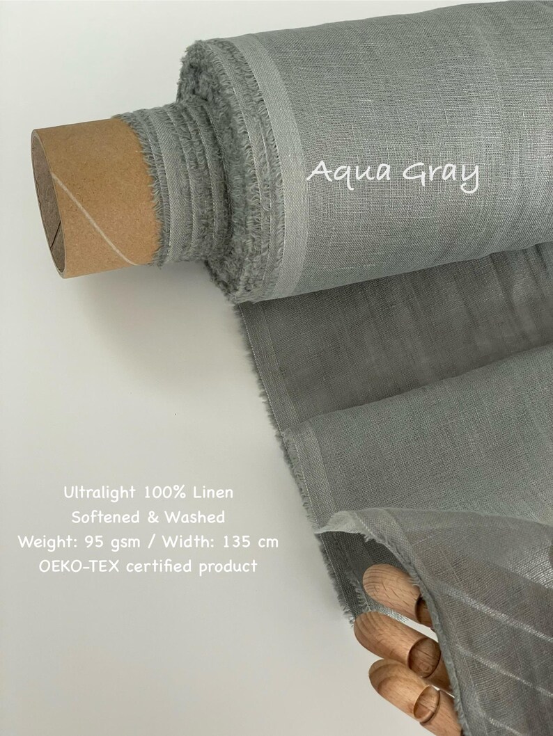 May include: A roll of aqua gray ultralight 100% linen fabric. The fabric is softened and washed, with a weight of 95 gsm and a width of 135 cm. The text "Aqua Gray" is written on the fabric. The product is OEKO-TEX certified.