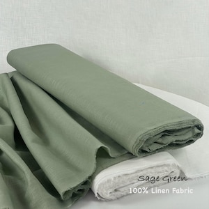 Könnte beinhalten: Eine Stoffrolle aus 100% salbeigrünem Leinen mit sichtbarer Webstruktur. Der Stoff ist gefaltet und drapiert und weist eine weiche, matte Oberfläche auf. Der Text "Sage Green 100% Linen Fabric" ist unten rechts aufgedruckt.