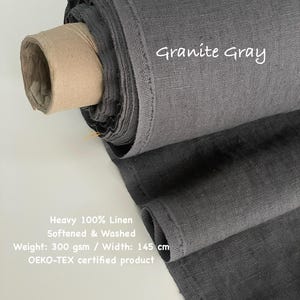May include: A roll of heavy, softened, and washed 100% linen fabric in Granite Gray. The fabric has a weight of 300 gsm and a width of 145 cm. The text "Granite Gray" is written on the fabric. The product is OEKO-TEX certified.