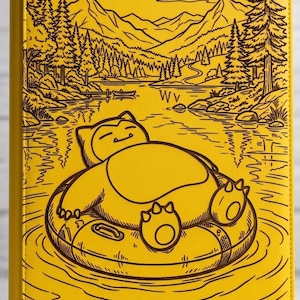 May include: A bright yellow binder featuring a dark brown line art illustration of a Snorlax floating on an inner tube in a lake surrounded by pine trees and mountains. The text "vaultx" is printed in the bottom left corner of the cover.