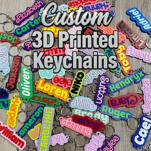 May include: A collection of custom 3D printed keychains in various bright colors, each featuring a unique name in raised lettering. The keychains are attached to silver metal split rings. The image includes the text Custom 3D Printed Keychains.