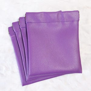 May include: Four purple leather coin purses stacked on top of each other. The purses have a zipper closure and a smooth, textured surface.
