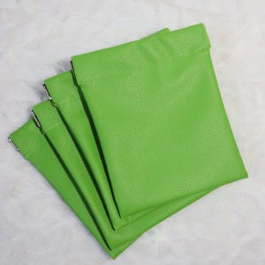 May include: Four green faux leather pouches with silver metal closures. The pouches are stacked on top of each other.