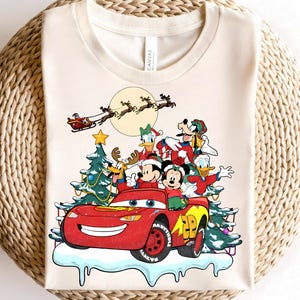 Pu&ograve; includere: T-shirt color crema con un design festivo con personaggi Disney. Topolino e Minnie, Paperino e Pippo sono in un'auto rossa con un albero di Natale. Babbo Natale vola nel cielo con le renne. Un numero 28 giallo &egrave; sull'auto.