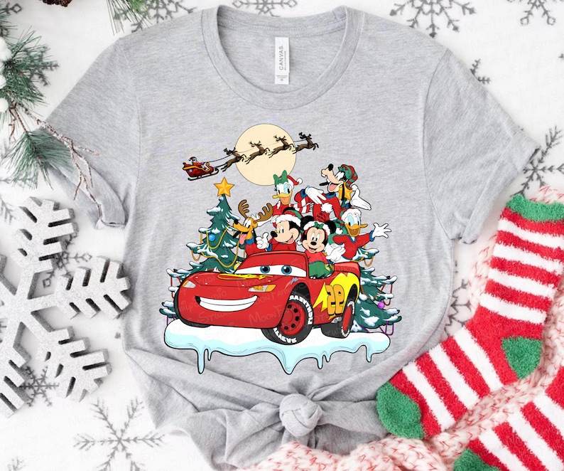 Pu&ograve; includere: T-shirt grigio chiaro con una grafica festiva di personaggi Disney in un'auto da corsa rossa, con un albero di Natale e la slitta di Babbo Natale sullo sfondo. Il design include Topolino e Minnie, Paperino e Pippo.