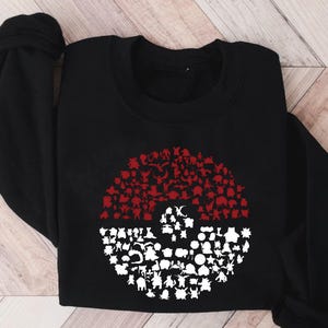 May include: Black sweatshirt with a red and white Pokeball design. The Pokeball is made up of many different Pokemon characters.