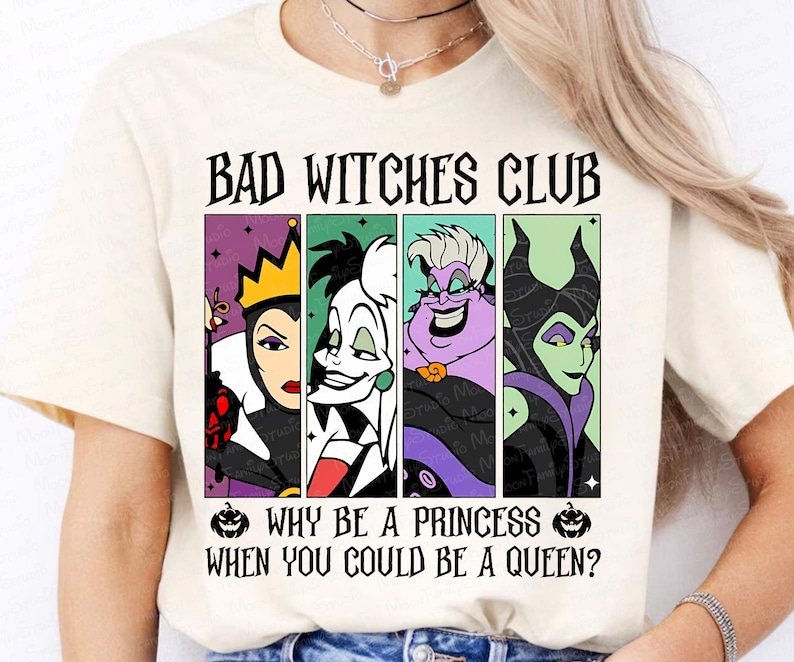 May include: Cream-colored t-shirt featuring the text "BAD WITCHES CLUB" above a graphic of four cartoon villains. Below the graphic, the text reads "WHY BE A PRINCESS WHEN YOU COULD BE A QUEEN?" The shirt has short sleeves.