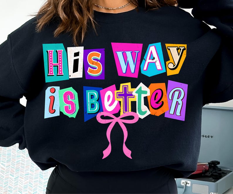 May include: Black sweatshirt with the text "His Way is Better" in colorful, cut-out style letters. A pink bow graphic is below the text. The sweatshirt is a casual, comfortable style.