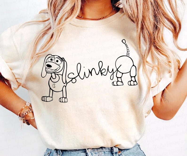 Peut inclure: T-shirt blanc avec un dessin au trait noir de Slinky Dog de la franchise Toy Story. Le texte "Slinky" est &eacute;crit en cursive.