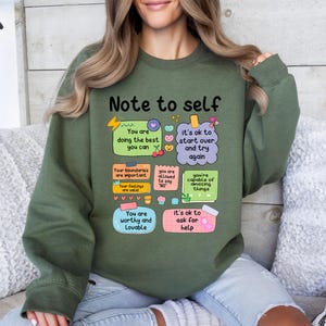 Może przedstawiać: Zielona bluza z napisem "Note to self" i inspirującymi wiadomościami na kolorowych karteczkach samoprzylepnych. Wiadomości obejmują "You are doing the best you can" i "You are worthy and lovable."