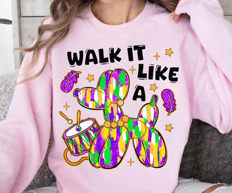 May include: A light pink sweatshirt with a colorful balloon dog design. The design includes a drum, stars, and the text "WALK IT LIKE A". The balloon dog is purple, green, and yellow.