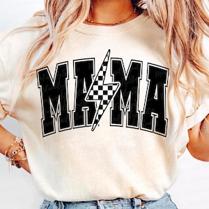 May include: A white t-shirt with a black graphic that says "MAMA" in a varsity style font with a black and white chequered lightning bolt in the centre.