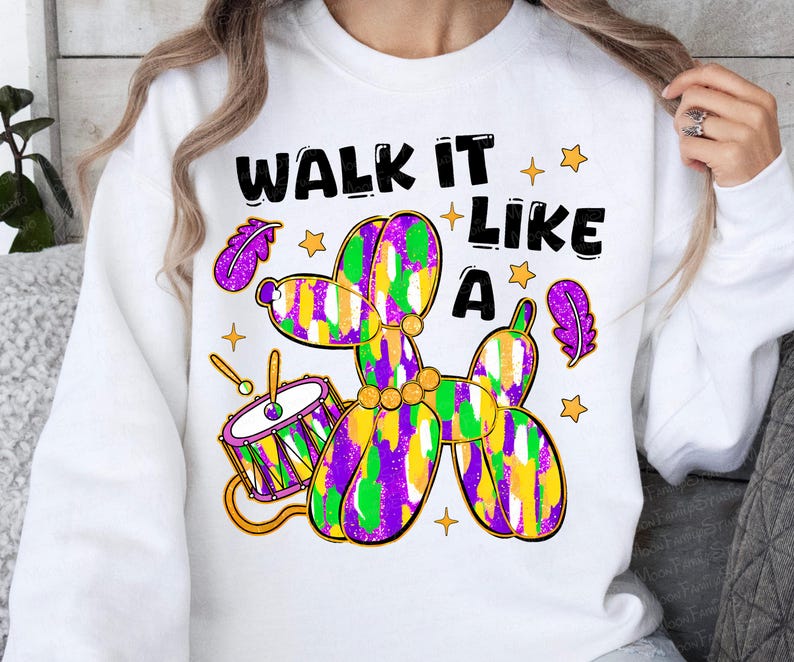 May include: White sweatshirt with the text "WALK IT LIKE A" above a colorful balloon animal dog, drum, stars, and feathers. The balloon animal is purple, green, and yellow. The drum is purple, gold, and white.