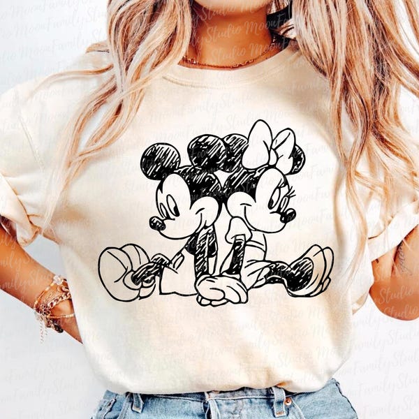 May include: Cream-colored t-shirt featuring a black and white sketch of Mickey Mouse and Minnie Mouse sitting back-to-back. The cartoon characters are in a relaxed pose, with Mickey wearing gloves and Minnie wearing a bow.