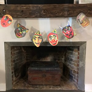Op de afbeelding: Een reeks vintage Halloween-maskers hangen boven een bakstenen open haard. De maskers zijn een duivel, een clown, een heks, een kat en een monster.