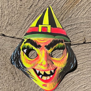 Op de afbeelding: Een vintage heksenmasker met een gele en zwarte puntmuts, rode en groene accenten en een enge, tandenrijke grijns.