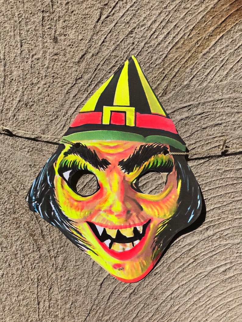 Op de afbeelding: Een vintage heksenmasker met een gele en zwarte puntmuts, rode en groene accenten en een enge, tandenrijke grijns.
