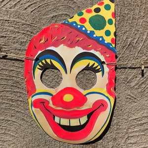 Op de afbeelding: Een kleurrijk papieren clownmasker met een rode neus, gele en blauwe ogen en een rode glimlach met witte tanden. Het masker heeft een gele, groene en rode stippenhoed.