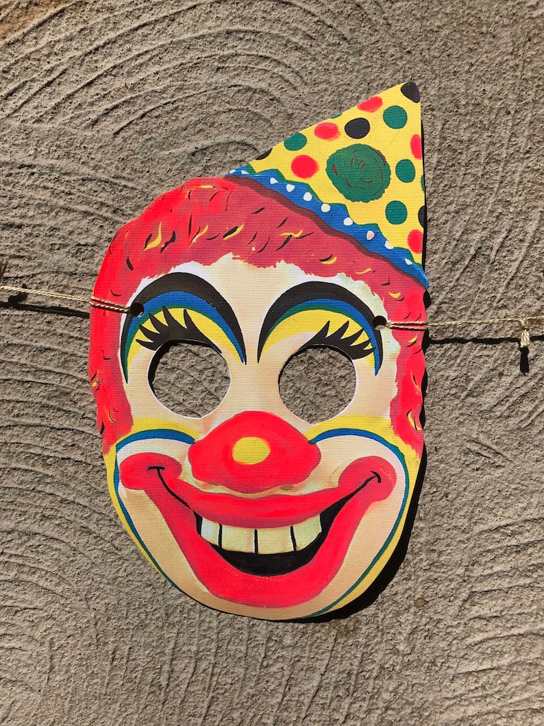 Op de afbeelding: Een kleurrijk papieren clownmasker met een rode neus, gele en blauwe ogen en een rode glimlach met witte tanden. Het masker heeft een gele, groene en rode stippenhoed.