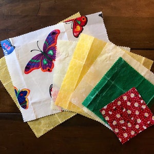 May include: A stack of colorful fabric squares with butterfly designs. The squares are made of different materials, including cotton, linen, and beeswax. They are perfect for wrapping food and storing leftovers.