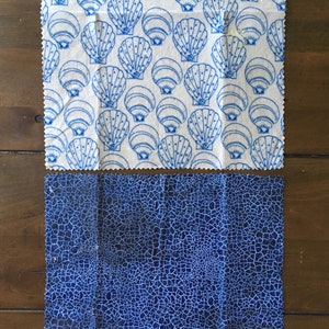 May include: Two blue and white fabric squares. The top square has a repeating pattern of blue seashells on a white background. The bottom square has a blue cracked pattern on a white background.