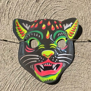 Op de afbeelding: Een zwart en groen papieren Halloween-masker van een kat met gele en rode details. Het masker heeft een wijd open mond met scherpe tanden en een zwarte neus.