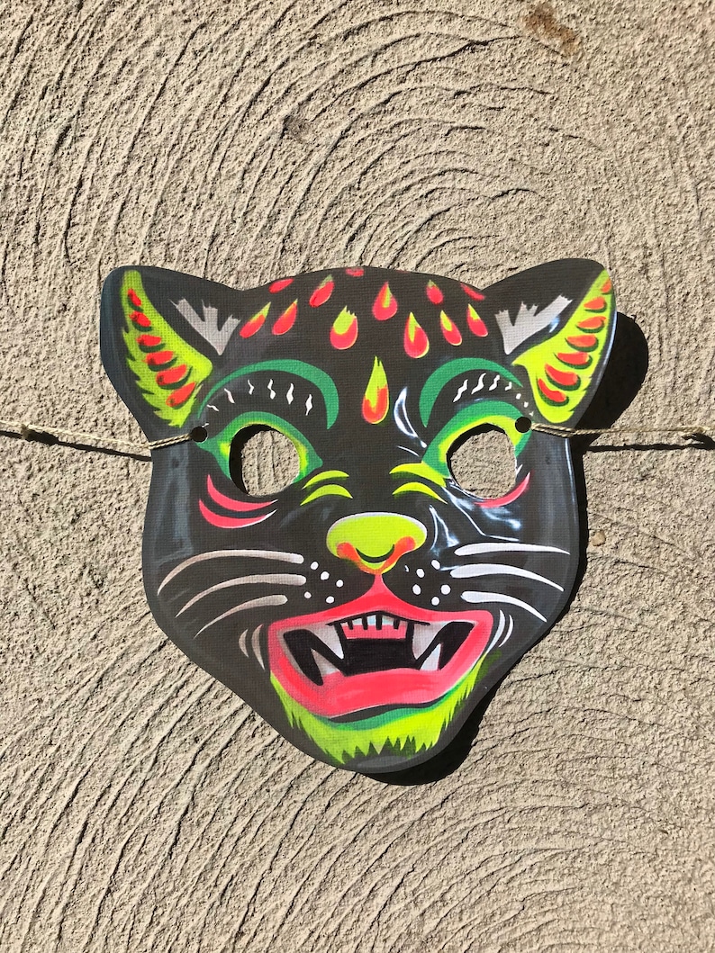 Op de afbeelding: Een zwart en groen papieren Halloween-masker van een kat met gele en rode details. Het masker heeft een wijd open mond met scherpe tanden en een zwarte neus.