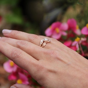 Woman wearing a Yellow gold engagement and wedding band with a diamond held by a rose. Two leaves and four diamonds accent the center. The bands curve to fit together