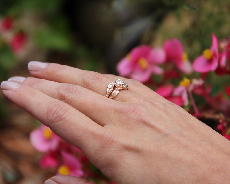 Woman wearing a Yellow gold engagement and wedding band with a diamond held by a rose. Two leaves and four diamonds accent the center. The bands curve to fit together