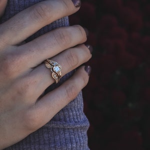 Woman wearing a Yellow gold engagement and wedding band with a diamond held by a rose. Two leaves and four diamonds accent the center. The bands curve to fit together