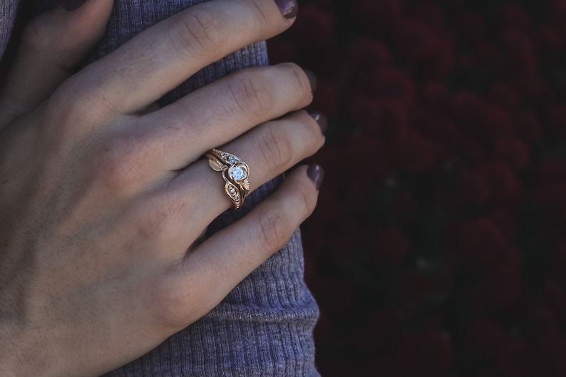 Woman wearing a Yellow gold engagement and wedding band with a diamond held by a rose. Two leaves and four diamonds accent the center. The bands curve to fit together