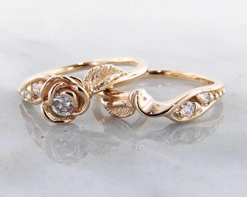 Two yellow gold rings, The engagement ring has a rose in the center, measuring approximately 1/4 inch The band is shaped in an S curve with a leaf on one side and two diamonds on the other. Matching wedding band also has a leaf and diamond accents