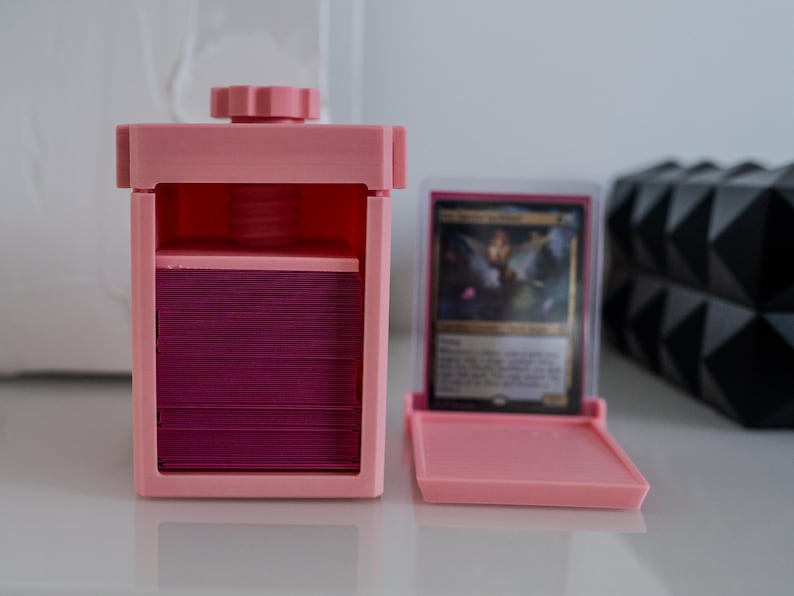 May include: A pink plastic card storage box with a clear lid and a compartment for holding cards. The box is open and a stack of cards is visible inside.