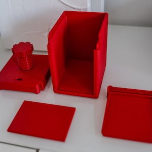May include: A red 3D printed puzzle box with a knob on top and a separate lid. The box is disassembled, showing the individual pieces.
