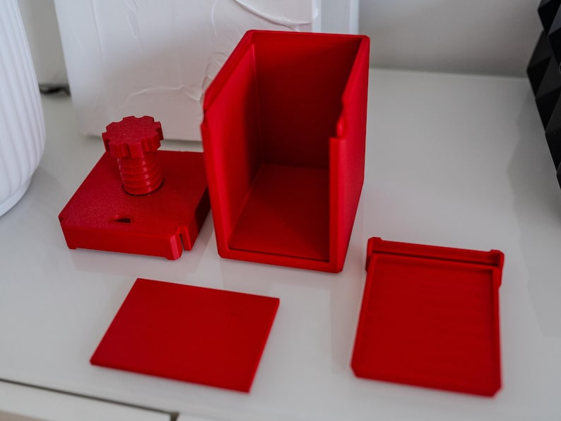 May include: A red 3D printed puzzle box with a knob on top and a separate lid. The box is disassembled, showing the individual pieces.