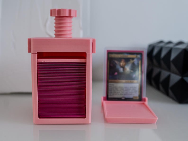 May include: A pink plastic card storage box with a screw-on top and a separate pink plastic card holder. The card holder has a clear window to view the cards inside.