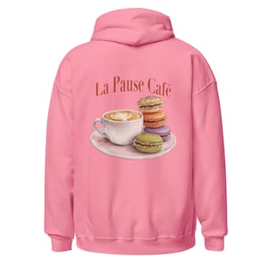 May include: Pink hooded sweatshirt with the text "La Pause Café" and a watercolor illustration of a coffee cup with latte art and a stack of macarons. The macarons are in shades of brown, orange, purple, and green.