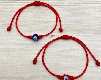 May include: Two red string bracelets with blue and white evil eye charms. The bracelets are adjustable and can be tied to fit any wrist size.