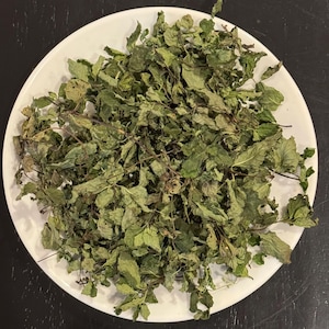 May include: A white plate filled with dried green mint leaves.