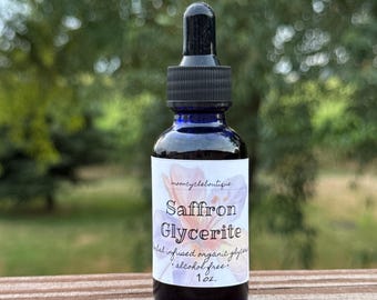 Może przedstawiać: Ciemnoniebieska szklana butelka z czarnym zakraplaczem. Etykieta głosi "Saffron Glycerite" i "herbal infused organic glycerin alcohol free 1 oz.". Butelka stoi na drewnianej powierzchni z rozmytym zielonym tłem.